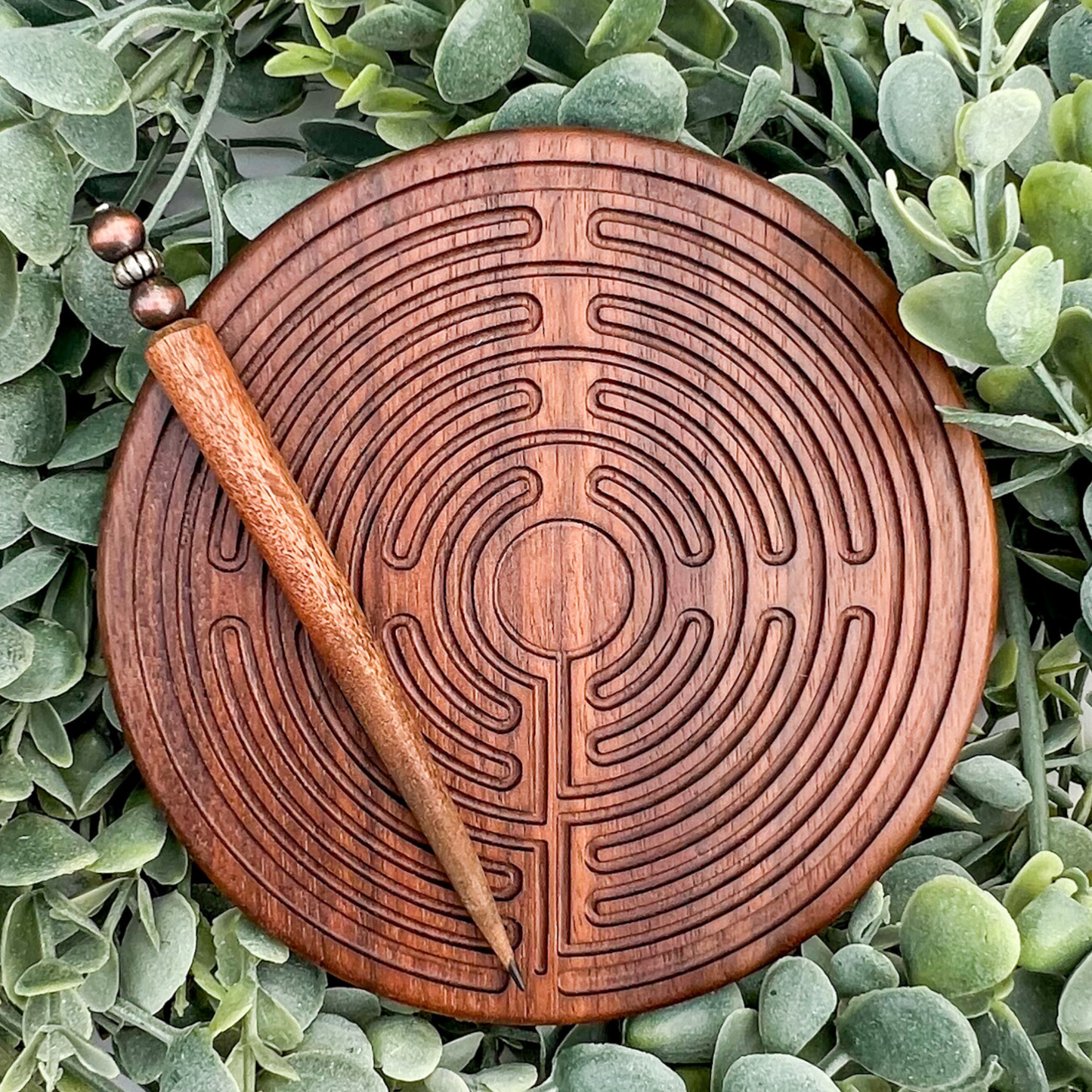 Wooden labyrinth disc with a wooden stylus on a bed of green leaves